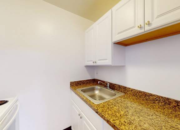 A kitchen with a granite counter top and white cabinets.