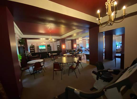 A room with a chandelier, tables, chairs, and a television.