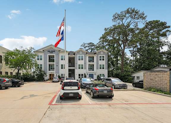 A white building with a flag on top and cars parked in front.