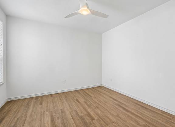 A room with a ceiling fan and wooden flooring.