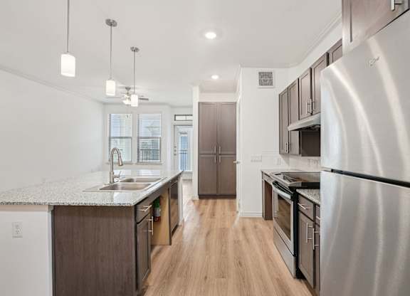 A modern kitchen with a refrigerator on the right and a sink with a window in the background.