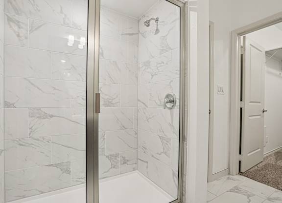 A white marble tiled bathroom with a glass door.