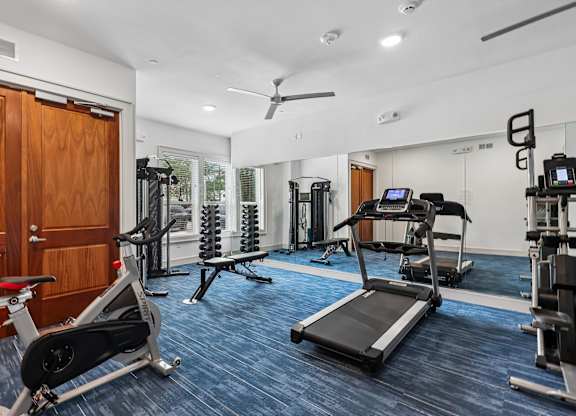 A gym with a variety of equipment including a treadmill, a stationary bike, and a weight bench.
