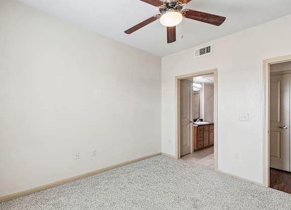 A room with a ceiling fan and a door leading to another room.