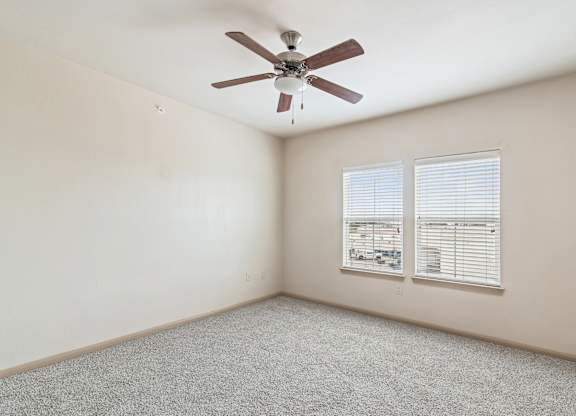 A room with a ceiling fan and two windows.