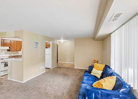 A living room with a blue couch and a kitchen area in the background.