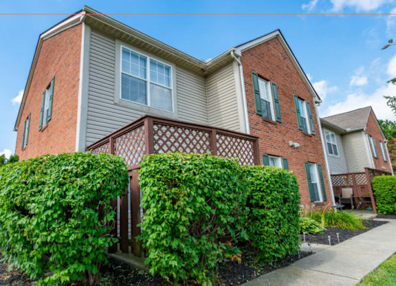 A two-story house with a red brick exterior and a balcony covered in green vines.