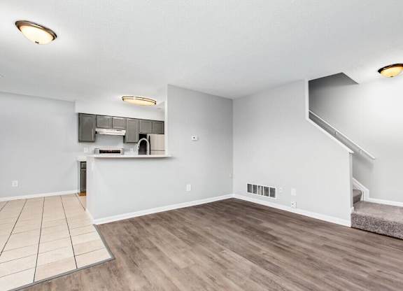A spacious room with wooden flooring and a staircase.