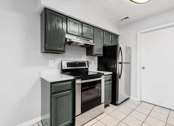 A kitchen with green cabinets and black appliances.