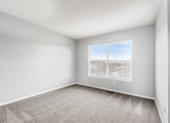 A room with a carpeted floor and a window with blinds.
