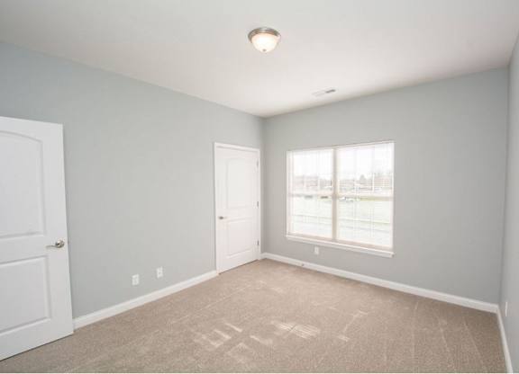A room with a carpeted floor and a window with blinds.