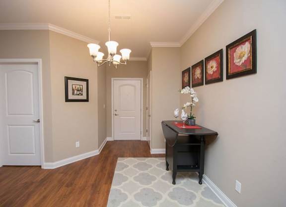 A hallway with a chandelier, a desk, and pictures on the wall.