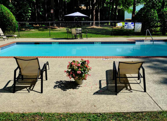 A pool with chairs and a vase of flowers.