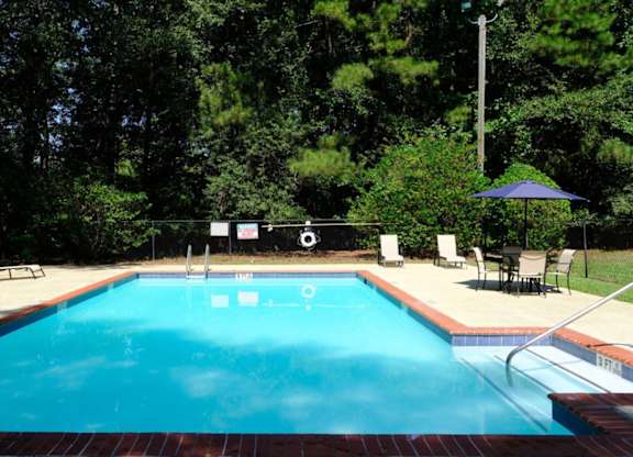 A pool surrounded by trees and chairs.