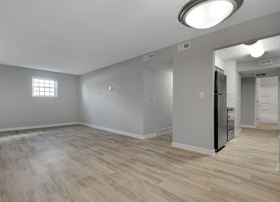 A spacious room with wooden flooring and a refrigerator in the corner.