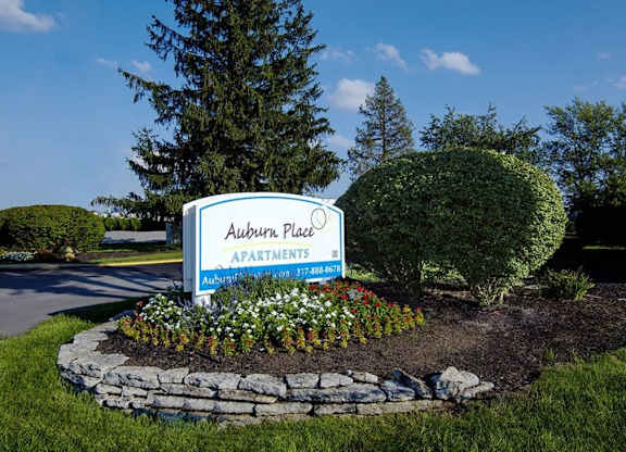 A sign for Auburn Place Apartments is surrounded by flowers and greenery.
