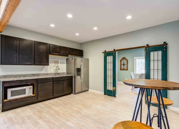 A kitchen with a wooden table and chairs, a refrigerator, and a microwave.