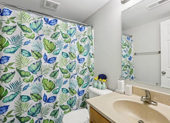 A bathroom with a green leaf patterned shower curtain.