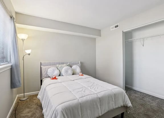 A bedroom with a white bed and a grey floor lamp.