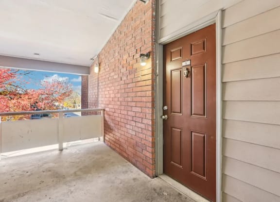 A brown door is on the right side of a room with a brick wall.