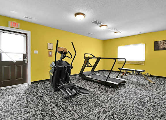 A gym with a treadmill, elliptical trainer and a weight machine.