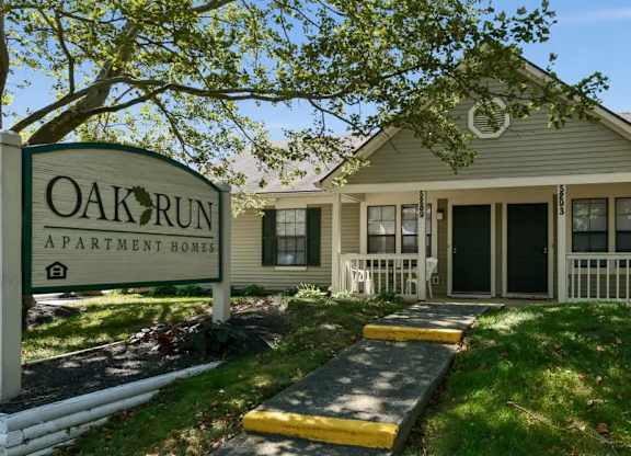 A sign that says Oak Run Apartment Homes in front of a house.