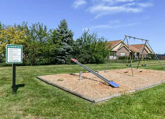 A swing set in a playground with a sign in the background.