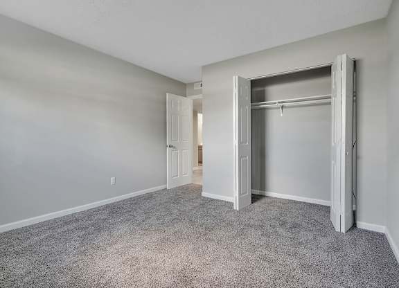 A room with a grey carpet and white walls with a doorway leading to another room.
