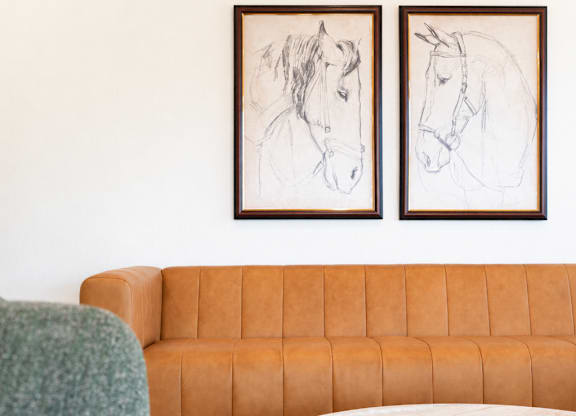 A living room with a brown couch, a green chair, and two framed pictures of horses on the wall.