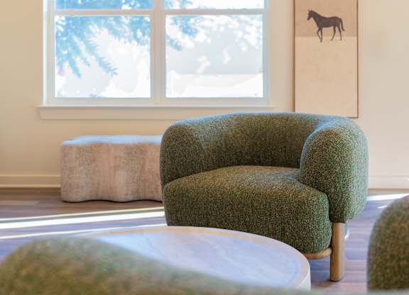 A green chair sits in front of a window in a room with a picture of a horse on the wall.