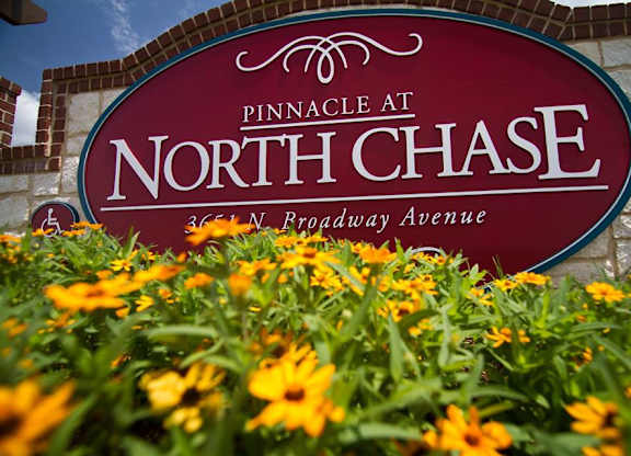 A sign for Pinnacle at North Chase is displayed in front of flowers.