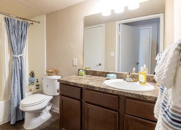 A bathroom with a white toilet, brown cabinets, and a white sink.