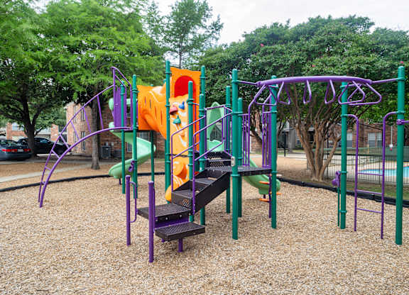 A playground with a purple and green structure and a yellow slide.