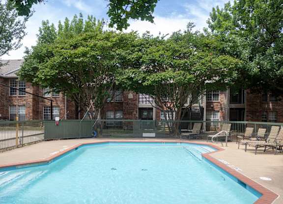 A small pool surrounded by trees and chairs.