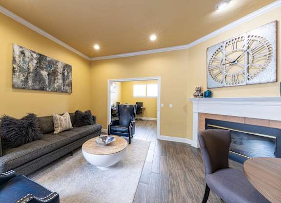 A living room with a grey couch, a coffee table, and a large clock on the wall.