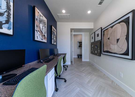 A room with a desk and chairs with a blue wall and artwork.