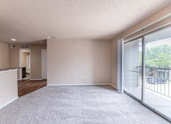 A spacious room with a carpeted floor and sliding glass doors leading to a balcony.