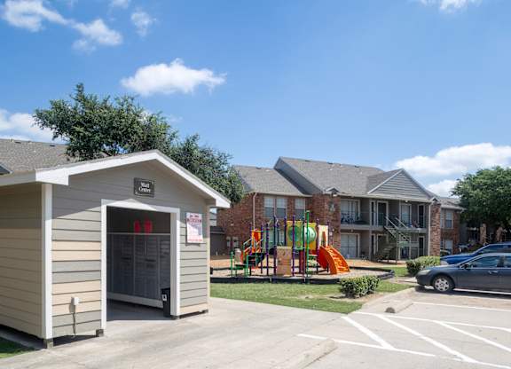 A small building with a red sign on the door is in front of a playground and a multi-story apartment building.