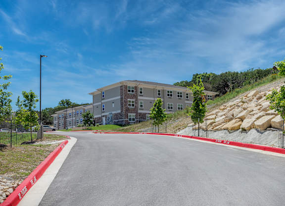 A road leads to a large building with a red curb on the side.