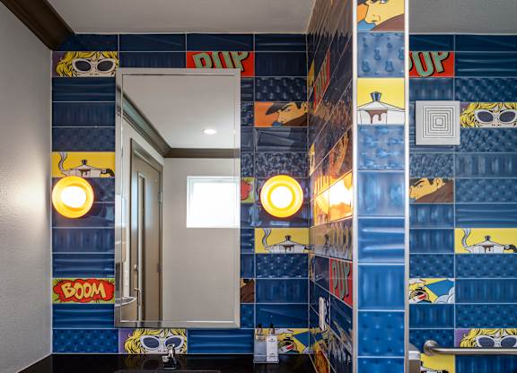 A bathroom with a sink and mirror with a blue tile wall.