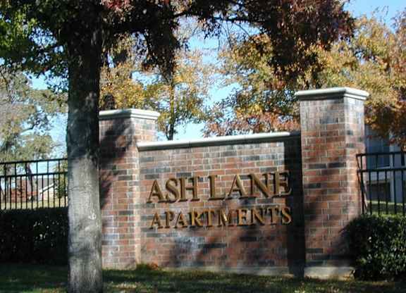 A sign for Ash Lane Apartments is displayed on a brick wall.