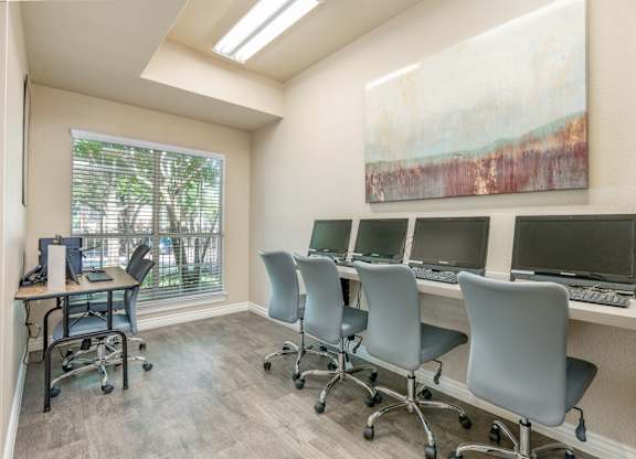 A room with a desk, chairs, and computers.