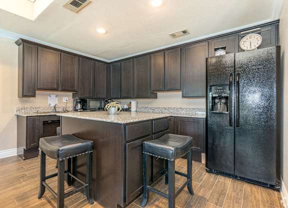 A kitchen with a black refrigerator and bar stools.