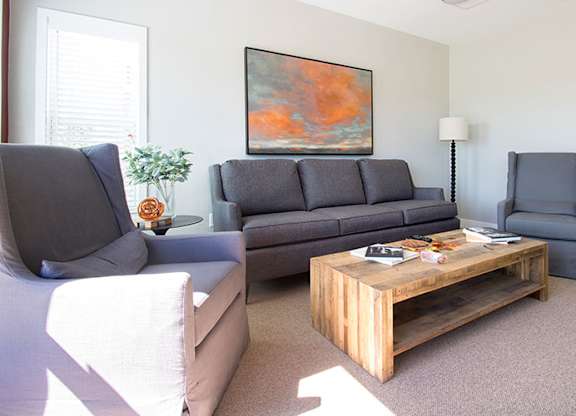 A living room with a grey couch, a wooden coffee table, and a painting on the wall.