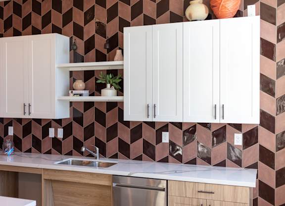 A kitchen with white cabinets and a brown tiled backsplash.