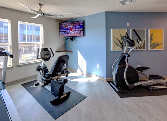 A room with a treadmill, a stationary bike, and a television playing a basketball game.