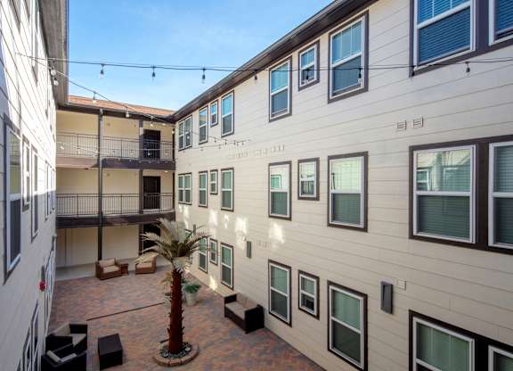 A courtyard with a palm tree and seating area between two buildings.