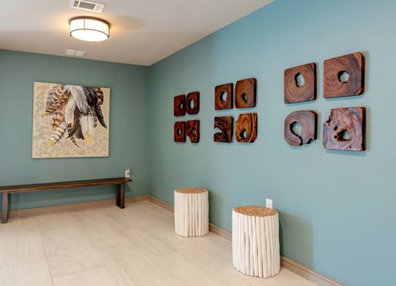 A room with a bench, two stools and a painting on the wall.
