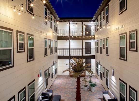 A courtyard with a palm tree and benches is surrounded by buildings.