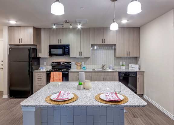 A kitchen with a black refrigerator and a granite countertop.
